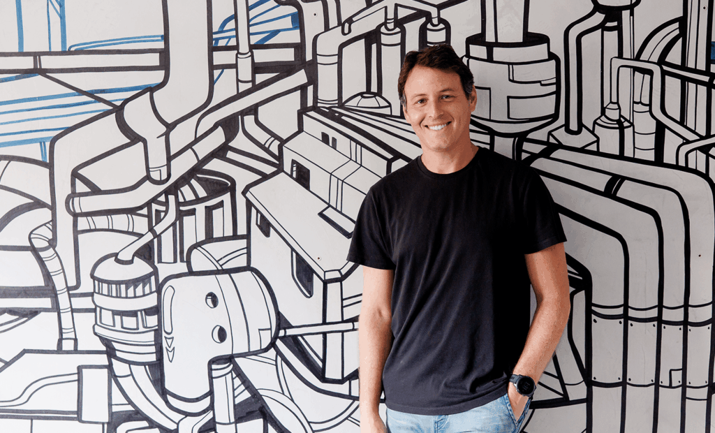 CVC Corp. Imagem do  Head de Impacto e Influência da EqualWeb, Jaques Haber. Um homem branco de cabelos pretos, vestindo uma blusa preta e calça jeans. Ele está encostado em uma parede com alguns desenhos. 
