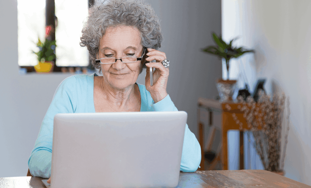 inclusão. Uma senhora de idade usando o telefone celular e mexendo no notebook.
