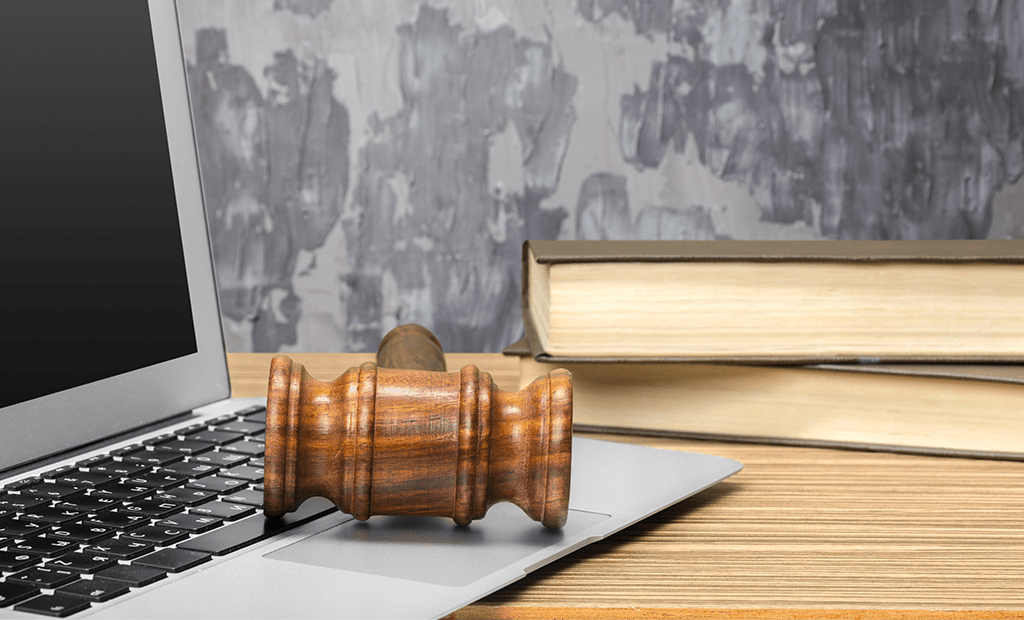 acessibilidade digital. Imagem de uma mesa com um notebook aberto e em cima do teclado um martelo da justiça.