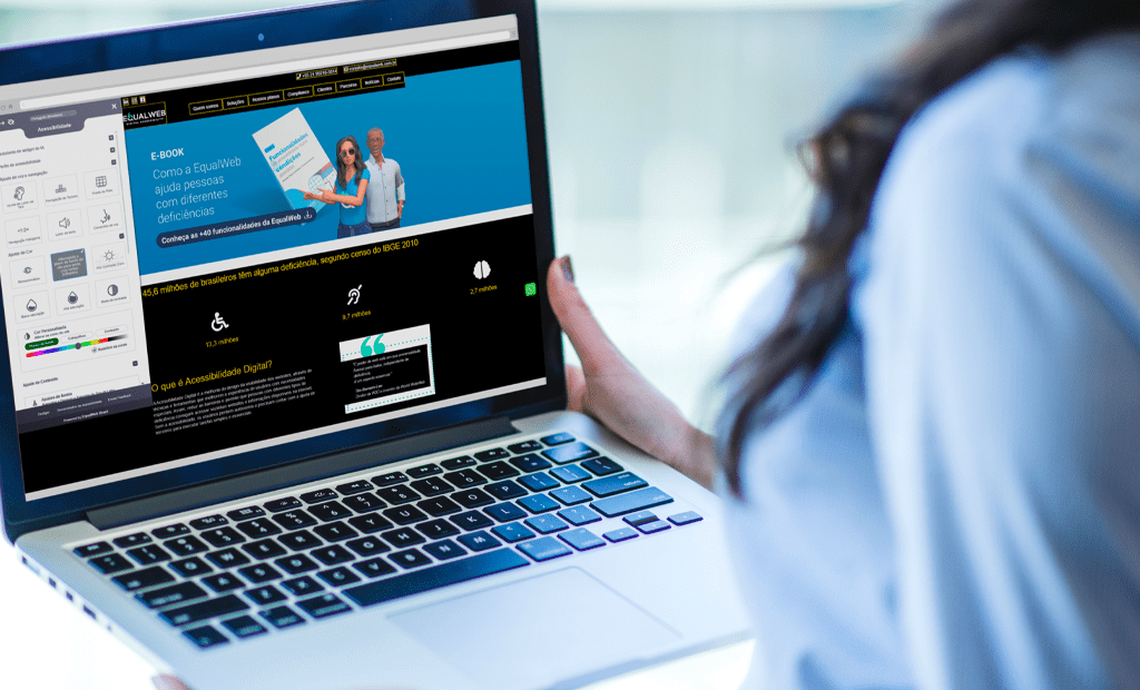 Leitores de tela. Pessoa segura um notebook com o site da EqualWeb aberto. A página exibe informações sobre acessibilidade digital e um banner com o título “Como a EqualWeb ajuda pessoas com diferentes deficiências”. O modo de acessibilidade do site está ativado, com várias opções visíveis no lado esquerdo da tela.
