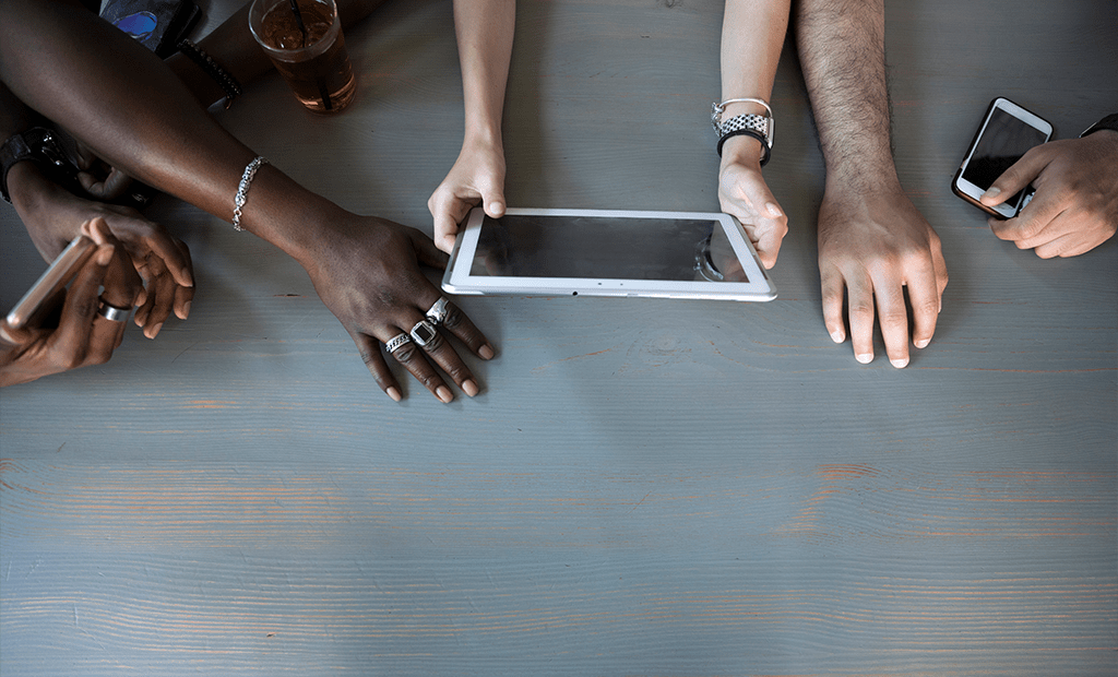 wcag. Diversas mãos sobre uma mesa de madeira segurando dispositivos móveis, como celulares e tablet