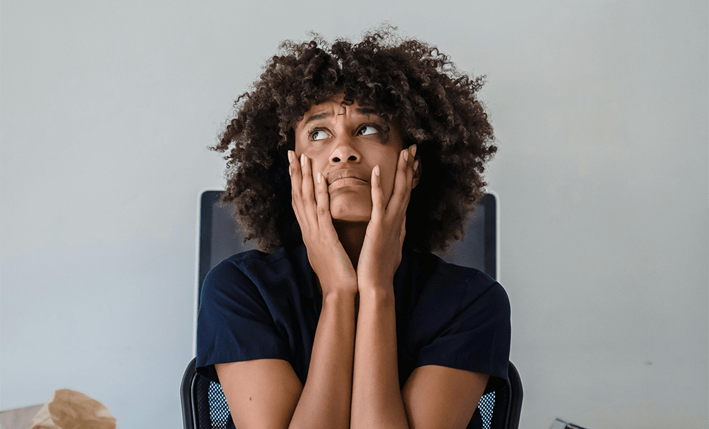 Acessibilidade digital no marketing. Mulher sentada com as mãos no rosto e expressão de preocupação, olhando para cima, em ambiente interno com fundo neutro.