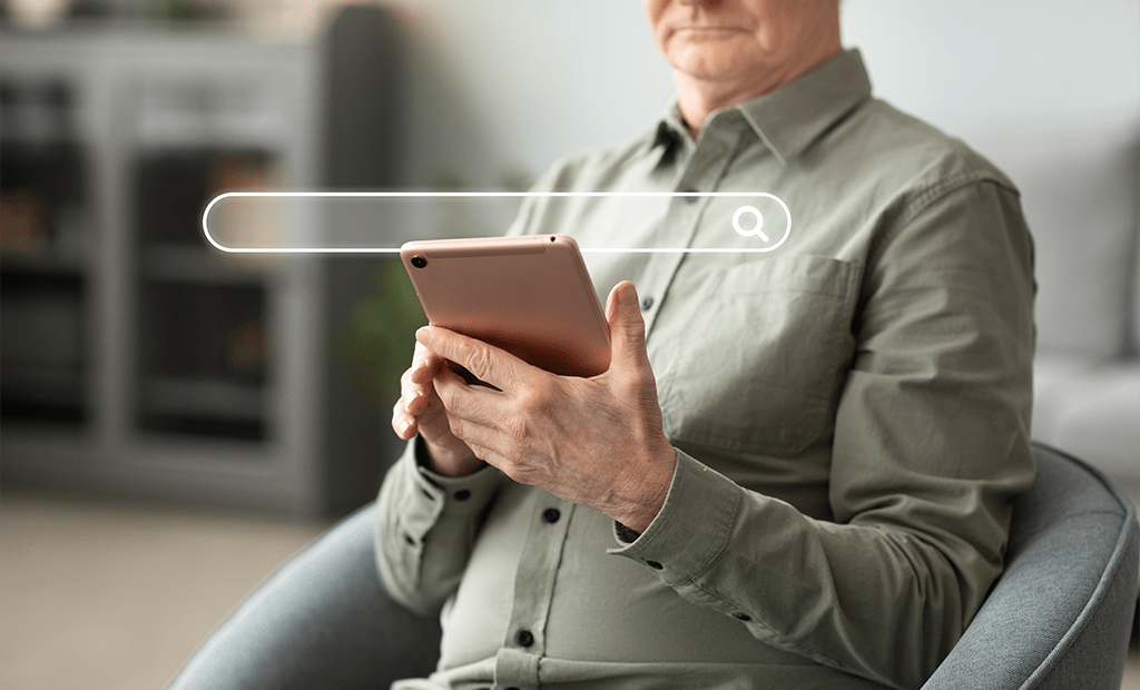 Acessibilidade digital no marketing. Homem mais velho usando tablet enquanto está sentado, com ícone gráfico de barra de busca sobreposto à imagem.